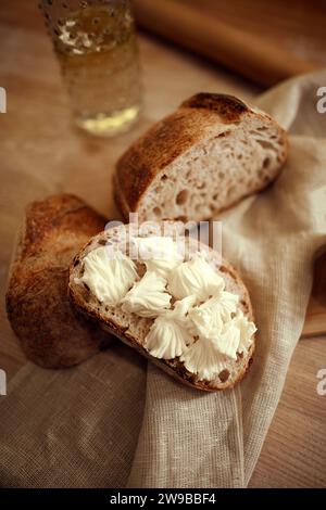 Pieces of delicious, hot homemade loaf of bread with fresh homemade butter lying in natural fabric on wooden table. Photo in selective focus. Stock Photo