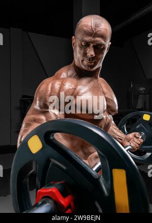 Professional weightlifter posing in the gym with a barbell in his hands. Classic bodybuilding. Mixed media Stock Photo