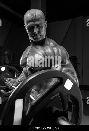 Professional weightlifter posing in the gym with a barbell in his hands. Classic bodybuilding. Mixed media Stock Photo