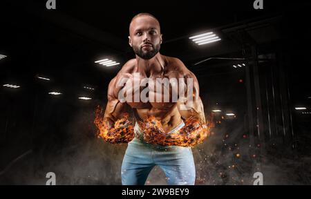 Professional athlete with fiery hands posing in the gym. Bodybuilding, fitness, sports concept. Mixed media Stock Photo