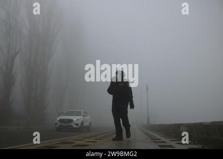 December 25, 2023, Srinagar Kashmir, India : A man walks along the shores of dal lake during a foggy and cold morning in Srinagar. The local Weather Department has forecasted that prevailing weather conditions to continue untill 31 December in the Himalayan region. The Weather department warns that there will be more decrease in temperatures and foggy weather will continue to engulf the region. Kashmir is currently in between a 40-day harsh winter period, the coldest part of winter that starts from 21 December to 29 January of every year. On December 25, 2023, Srinagar Kashmir, India. (Photo B Stock Photo