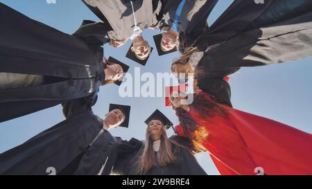 College graduates in a circle stand hugging each other. Stock Photo