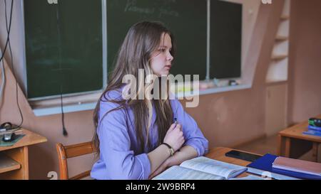 A schoolgirl in the role of a teacher sits at her desk. Stock Photo