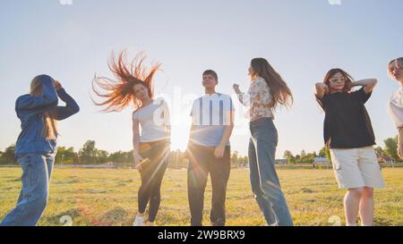 Funny jolly friends dancing in the city meadow in the evening. Stock Photo