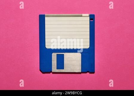 Top view of blank paper with lines stuck on blue floppy disk on pink background Stock Photo