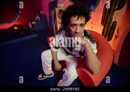 Man sitting in armchair holding hand on chin with thoughtful facial expression looking at camera Stock Photo