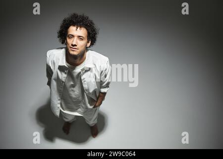 Guy in white outfit posing with hands in pockets looking at camera against gray studio background Stock Photo