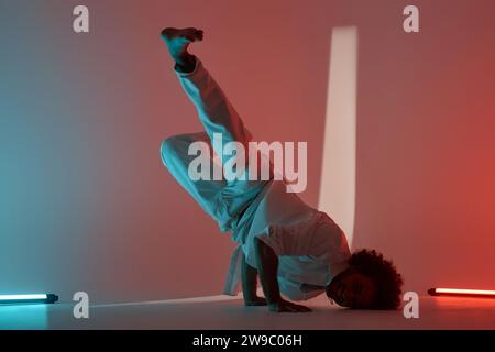 Full shot of young breakdancer doing handstand posing for camera in neon lit studio Stock Photo