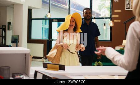 Receptionist providing luxury service to travellers checking in at exotic summer resort, travelling on honeymoon. Tourists with tropical clothes registering at front desk in lobby. Stock Photo