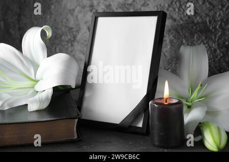 Blank funeral frame, Holy Bible, burning candle and beautiful lily flowers on black background Stock Photo