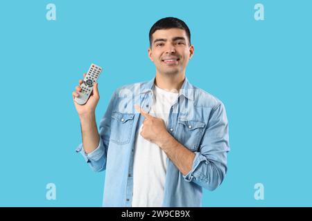 Handsome young man pointing at TV remote control on blue background Stock Photo