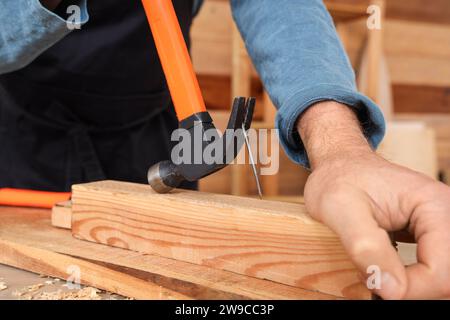 Mature carpenter pulling out nail from wooden plank at table in shop, closeup Stock Photo