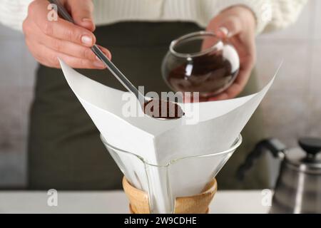 Making drip coffee. Woman adding ground coffee into chemex coffeemaker with paper filter, closeup Stock Photo