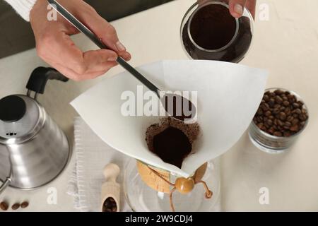 Making drip coffee. Woman adding ground coffee into chemex coffeemaker with paper filter at white table, closeup Stock Photo
