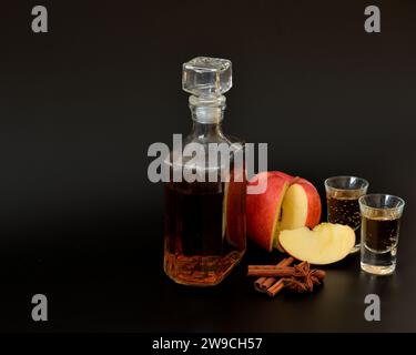 Homemade apple liqueur with cinnamon and anise in a bottle and two glasses on a black background. Close-up. Stock Photo