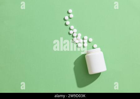 The white pill spilled out of a bottle of overturned bright white medicine bottle without label on green background. Copy space for design, drug adver Stock Photo