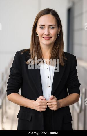Attractive dark-haired businesswoman in office suit looks at camera Stock Photo
