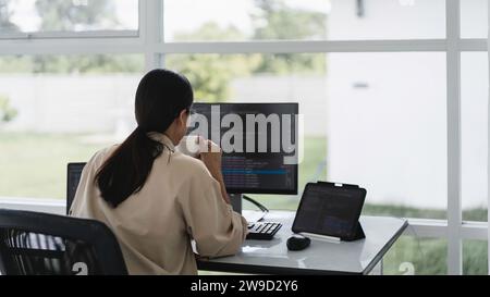 Developer programmer drinking coffee and checking code on monitor for programming to developing web. Stock Photo