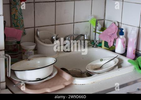 Dirty dishes in sink waiting to be washed. Dirty sink in apartment kitchen. Unsanitary conditions. Old dishes. Dirt everywhere. No water Stock Photo