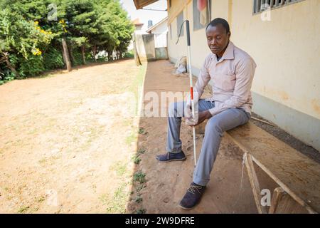 Blind man sitting on a wooden bench holding his white cane. Stock Photo