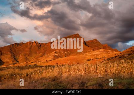 Red sunlit mountain at sunset under stormy skies in Lesotho Stock Photo