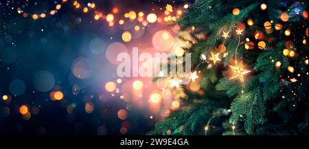 Christmas Tree With Lights In Blue - Stars Hanging On Fir Branches With Glittering And Bokeh In Abstract Defocused Background Stock Photo