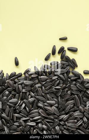 Unhulled black sunflower seeds on plain yellow background Stock Photo