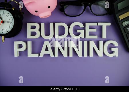 Budget Planning alphabet letters with piggy bank, alarm clock, calculator top view on purple background Stock Photo