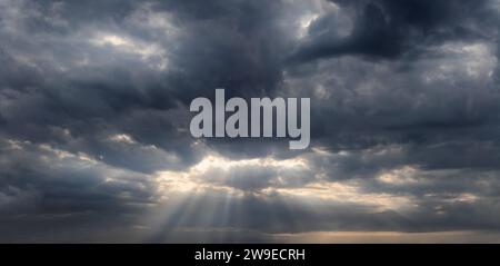 Sky background with sun rays shining through the dark rainy clouds. Stock Photo