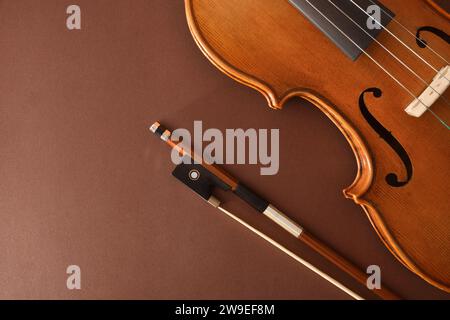 Traditional stringed violin and bow placed diagonally on isolated gradient brown background. Top view. Stock Photo