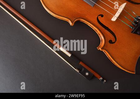 Traditional stringed violin and bow placed diagonally on isolated gradient black background. Top view. Stock Photo