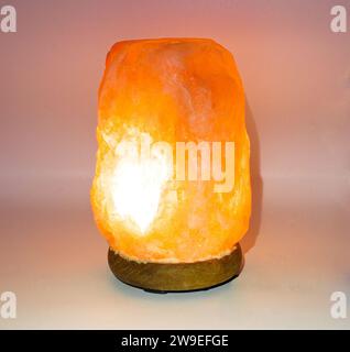Himalayan pink salt lamp with orange red glow isolated on light background which can boost mood, improve sleep, ease allergies, reduce anxiety and cle Stock Photo