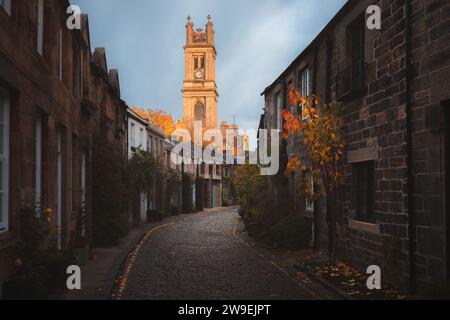 Golden sunset or sunrise light over the picturesque and quaint Circus Lane and St Stephen's Church clock tower with autumn colours in Edinburgh, Scotl Stock Photo