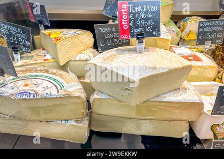 Italy - December 24, 2023: wheels of cheese cut and displayed with prices in food market window counter, typical Italian cheeses from Piedmont Stock Photo