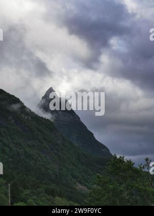 A scenic landscape featuring a mountain partially obscured by a foggy mist and fluffy clouds, with a quaint house in the foreground Stock Photo