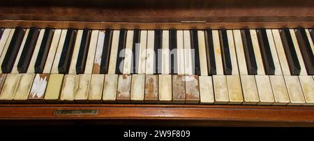 Old wooden upright grand piano black and white keys with detailed real ivory inlays with some missing on late 1800s instrument, worn, broken, damaged Stock Photo