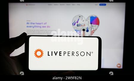 Person holding smartphone with logo of conversational commerce company LivePerson Inc. in front of website. Focus on phone display. Stock Photo