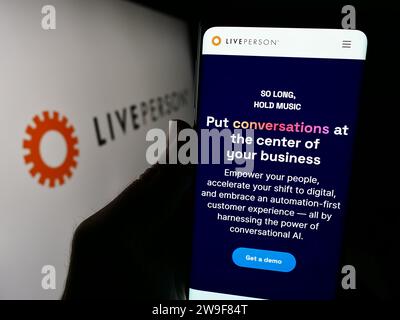 Person holding smartphone with webpage of conversational commerce company LivePerson Inc. in front of logo. Focus on center of phone display. Stock Photo
