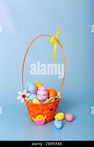 Wicker basket filled with decorative multi colored eggs on a light blue background Stock Photo