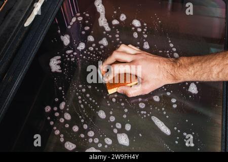 Male hand scrubbing oven glass with a sponge, home cleaning Stock Photo