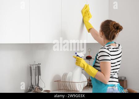 Woman in yellow rubber gloves cleaning cupboards in modern kitchen Stock Photo