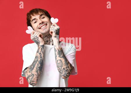 Handsome young man with paper hearts on red background Stock Photo