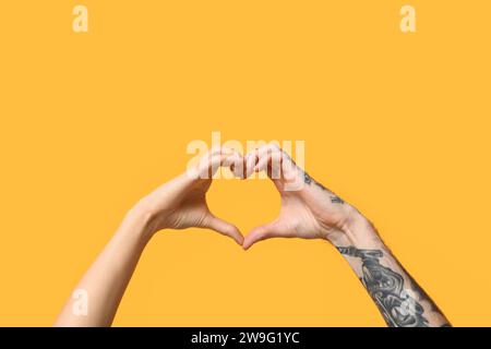 Woman and man making heart with their hands on yellow background Stock Photo
