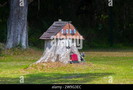 old tree stump turned into a garden fairy gnome house in the middle of Grass field with tiny bigfoot Stock Photo