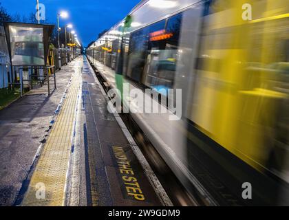 A passenger commuter train passing through Burgess Hill,railway station platform at speed during evening, with “Mind the Step” written on platform Stock Photo