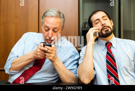 Two lazy businessmen using their phones instead of working Stock Photo