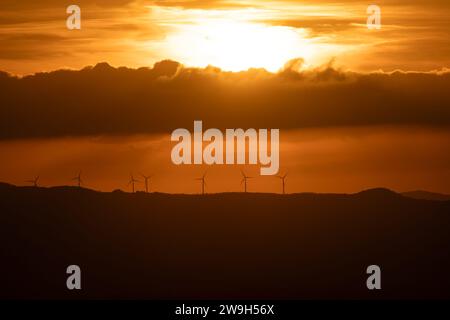 silhouette of wind turbines in the mountains under the dramatic sky at sunset Stock Photo