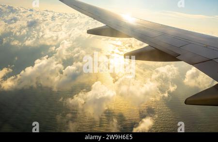 Airplane wing,  clouds shadows on water. Shadow of a cloud on water sea, airplane window view of rippled water with sun rays gleaming through clouds Stock Photo