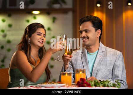 Indian Romantic couples champagnes wine glasses during candlelight dinner at restaurant - concept of date night, anniversary or valentines day Stock Photo