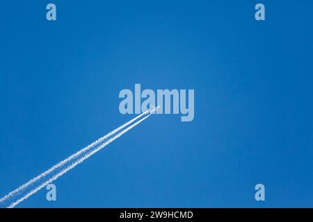 Air pollution from plane contrails during travel high overhead in a clear blue sky Stock Photo
